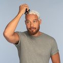 Man met stoppels en baard scheert zijn hoofd met een zwart Remington scheerapparaat met 5 scheerkoppen, bedekt met scheerschuim.