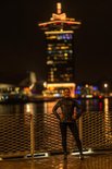 Vrouw poseert 's nachts voor een verlicht gebouw, draagt zwart hardloopjack met reflecterende print.