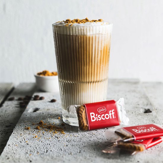 Glaasje met gelaagde koffie met schuim en gemalen koekjes, met twee verpakte Lotus Biscoff koekjes.