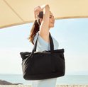Mannequin portant un haut bleu clair porte un sac fourre-tout noir sur l'épaule au bord de la mer.