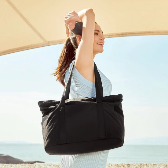 Mannequin portant un haut bleu clair porte un sac fourre-tout noir sur l'épaule au bord de la mer.