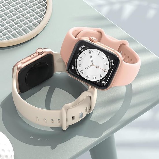 Twee Apple Watches, één met een lichtroze bandje en de ander met een zandkleurig bandje, op een grijze tafel.