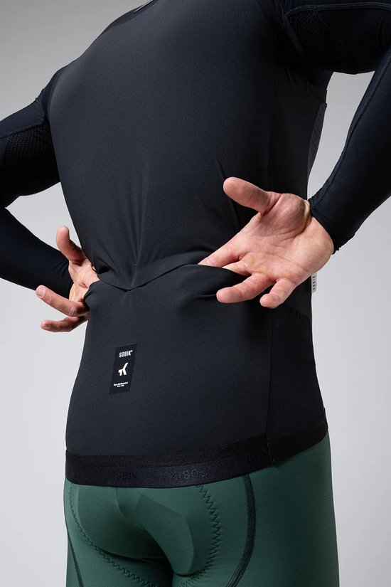 Model die een zwart GOBIK fietsshirt met lange mouwen en groene fietsbroek van achteren laat zien.