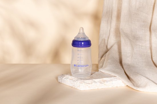 Een Lansinoh babyfles van 240 ml met paarse ring en Natural Wave speen, staand op een decoratief steen.
