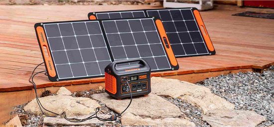 Twee Jackery SolarSaga 100 zonnepanelen, zwart met oranje accenten, verbonden met een oranje Jackery powerstation op een stenen ondergrond.