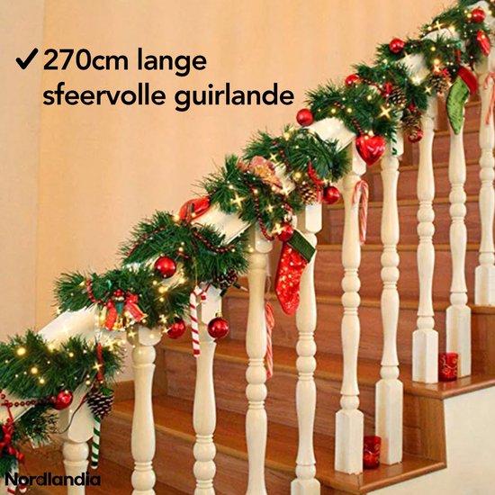 Kerstslinger van 270 cm met kerstballen, dennenappels, kerstkousen, lolly's en lichtjes, om een trapleuning gewikkeld.