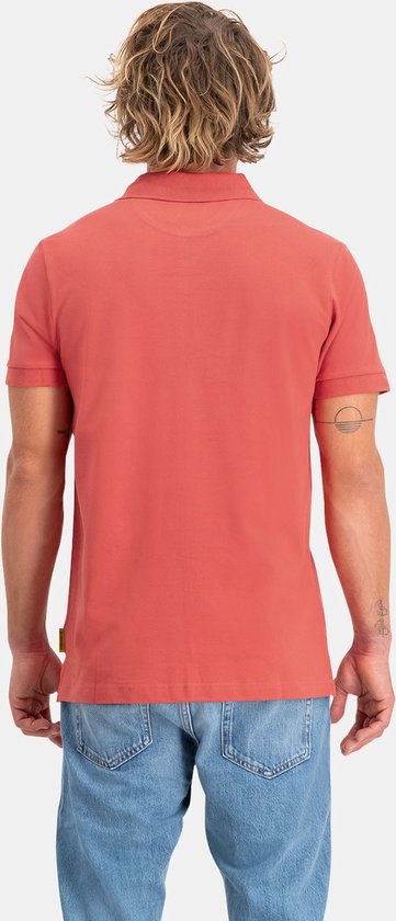 Man, van achteren gezien, met steil, golvend blond haar, een rood poloshirt met korte mouwen en lichtblauwe jeans.