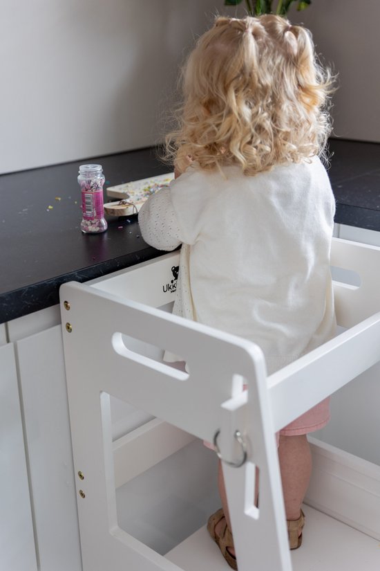 Wit kinderkeukentje met een meisje dat aan het knutselen is, met krullend blond haar, wit vestje en roze broekje.