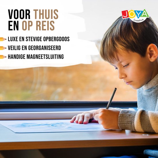 Jongetje in een grijze trui tekent geconcentreerd op papier, naast een raam. Een zwarte, luxe doos met kleurpotloden is op de achtergrond.