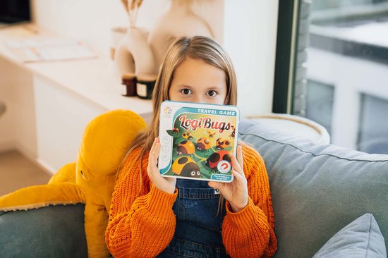Une jeune fille tenant la boîte de jeu LogiBugs, assise sur un canapé avec une grosse pieuvre jaune.