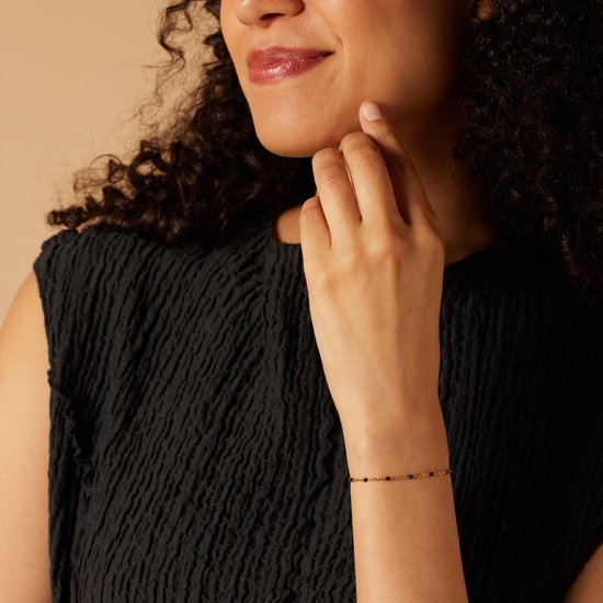 Model draagt gouden armband met schakels en zwarte kraaltjes.