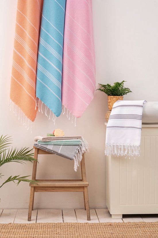 Hangende hamamdoeken in oranje, blauw, roze. Gestapelde doeken in grijs, beige, mintgroen. Witte doek met strepen.