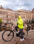 Jong meisje in fluoriserende gele regenjas en grijze regenbroek, staand op een fiets versierd met bloemen.