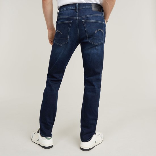 Achterkant van man met donkerblauwe G-Star 3301 slim jeans met lichte wassing en het kenmerkende G-Star logo op de achterzak.