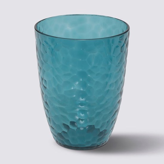 Blauw transparant drinkglas met hamerslag textuur, op grijze achtergrond.