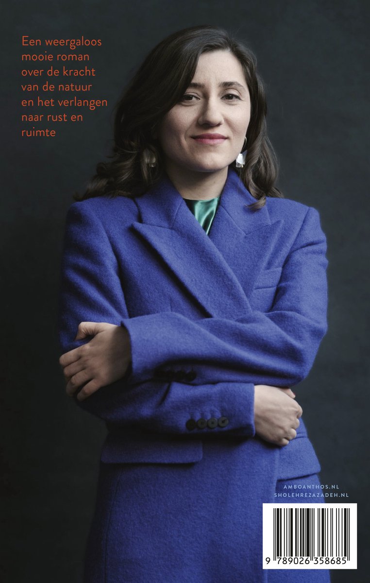 Een vrouw in een blauw mantelpak staat met gekruiste armen. De achtergrond is donker.
