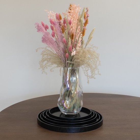 Zwarte ronde dienbladen gestapeld met een glazen vaas gevuld met roze en oranje gedroogde bloemen.