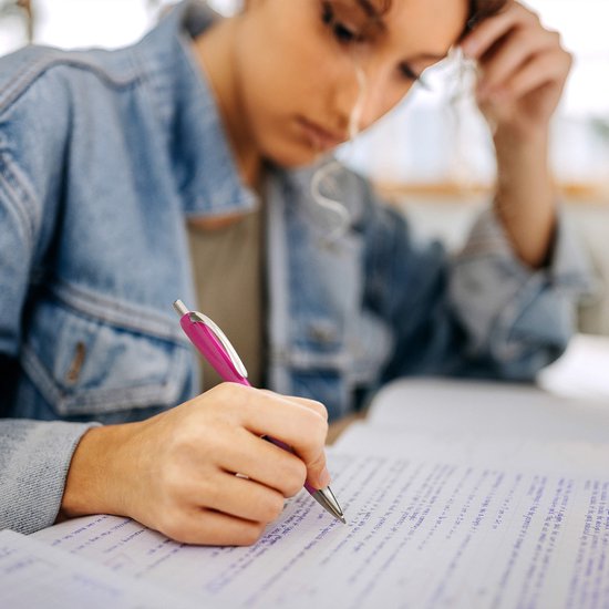 Close-up van een jonge vrouw in een spijkerjack die met een roze pen in een notitieboekje schrijft.