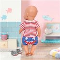 Baby Born pop van achteren gezien, met rood-wit gestreept shirt en blauwe broek met haaientanden. Draagt grijze haaienschoentjes.