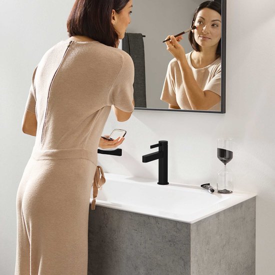 Matzwarte wastafelkraan naast een witte wasbak, een vrouw brengt make-up aan.