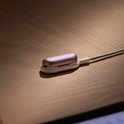 Paars PLAUD NotePin-apparaat op een houten tafel, aangesloten op een oplaaddock met kabel.