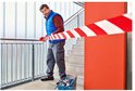 Man in blauw vest zet rood-wit waarschuwingslint uit bij een trap.