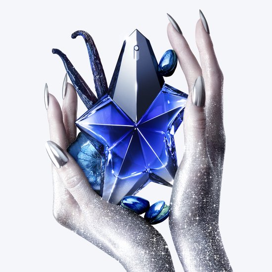Geglitterde handen houden een blauw Mugler Angel Stellar parfumflesje vast, omringd door vanillepeulen en macarons.