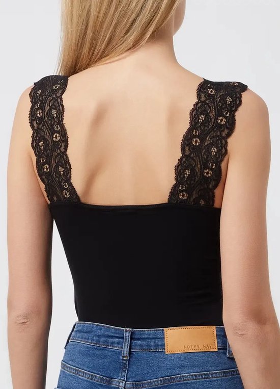 Model draagt een zwart hemd met kanten bandjes over de schouders, gecombineerd met een blauwe jeans.