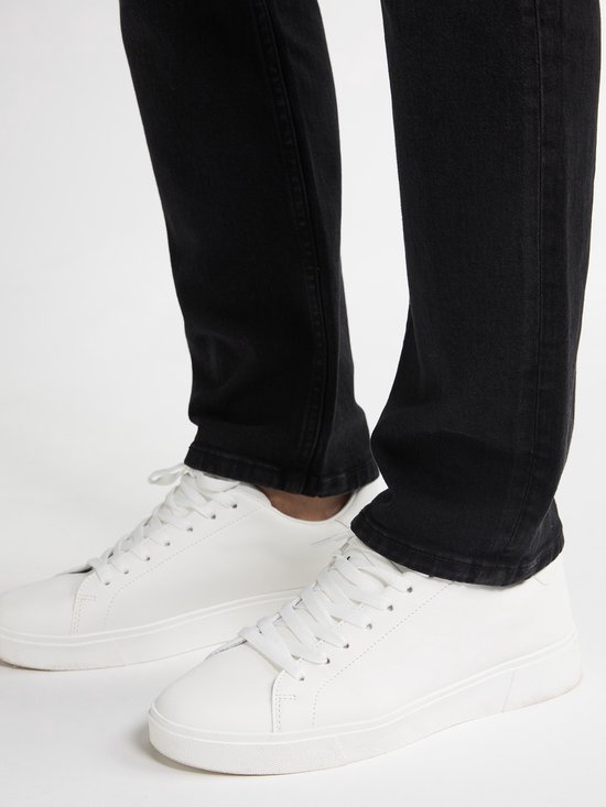 Voeten van een man in zwarte jeans en witte sneakers.