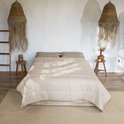 Gedrapeerd, lichtbruin, gewatteerd dekbed op een houten bed in een bohemian slaapkamer.