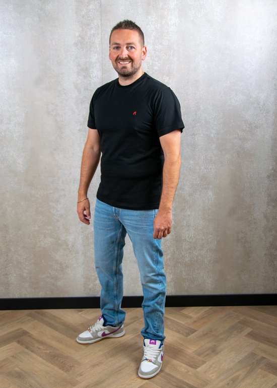Homme avec t-shirt noir et jean Replay bleu clair, debout.