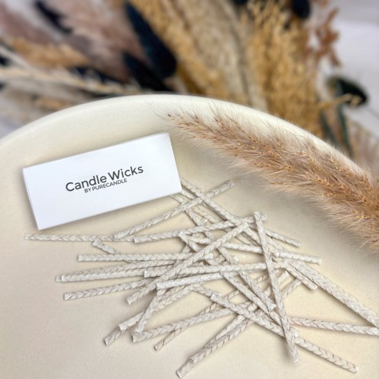 Een doosje met 'Candle Wicks BY PURECANDLE' en een stapel gevlochten lonten op een crème-kleurige ondergrond, met gedroogde grassen op de achtergrond.
