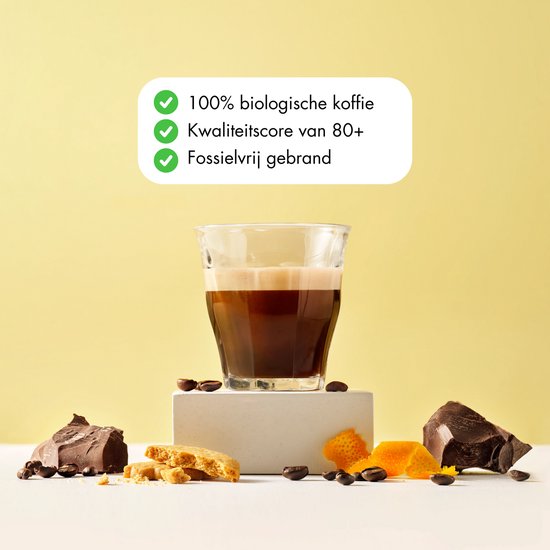 Glas espresso met schuim, omringd door stukken pure chocolade, stukjes koek en sinaasappelschil. Tekst: '100% biologische koffie', 'Kwaliteitsscore van 80+', 'Fossielvrij gebrand'.