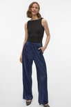 Model draagt een donkerblauwe, glanzende, geplooide broek met wijde pijpen.