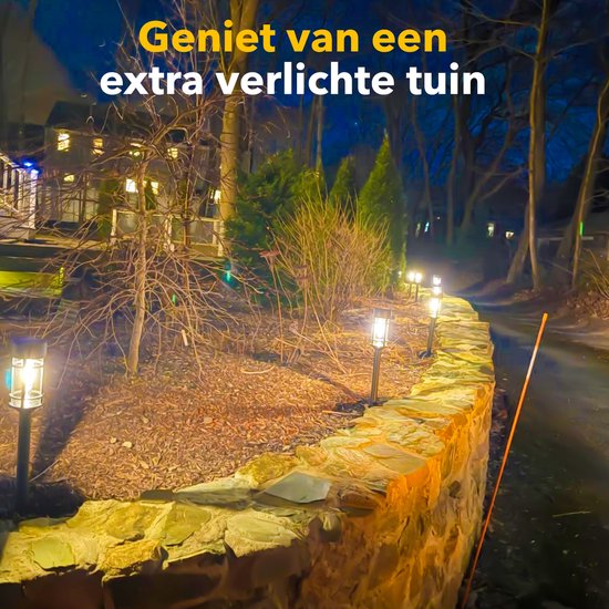 Donker tuinpad verlicht door meerdere solar fakkels langs een stenen muur.