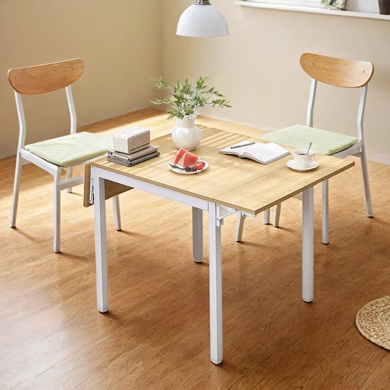 Table pliante en bois avec pieds blancs, deux chaises avec coussins vert clair, vase avec fleurs, livre et tranches de melon.