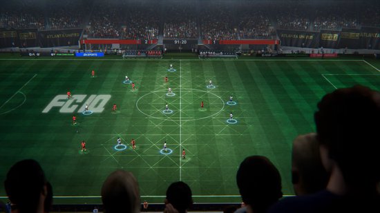 Vogelperspectief van voetbalwedstrijd in FC25 game met spelers in wit en oranje op groen veld.