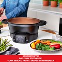 Zwarte multicooker met een stoomrek en gestoomde groenten zoals asperges, broccoli en paprika. Stoomfunctie voor vitamines.