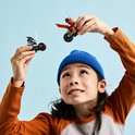 Kind met blauwe muts houdt twee LEGO Ninjago speelgoedmotoren omhoog, één rode en één blauwe.