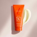 Oranje Lancaster tube met SPF 50 body milk, met een witte crème-achtige textuur ernaast.