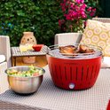 Rode LotusGrill met gegrilde kip en een salade op een terras.