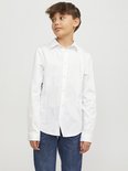 Un garçon porte une chemise blanche à manches longues et un jean.