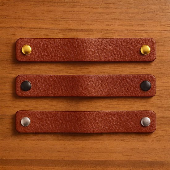 Drie bruine leren handgrepen met gouden, zwarte en zilveren knoppen, op houtnerf.