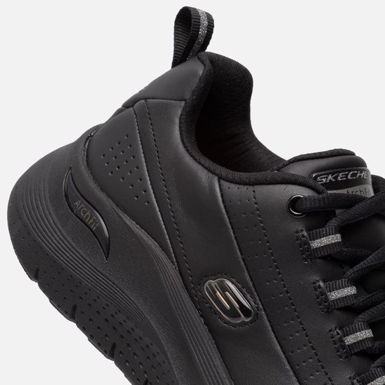 Close-up van een zwarte sneaker met 'Arch Fit' tekst op de zijkant en zilveren details.