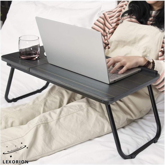 Vrouw op bed met laptop en glas op een donker houtnerf laptoptafel.