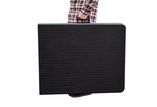 Persoon draagt een zwarte, inklapbare tafel met wickerlook textuur in opgevouwen toestand.