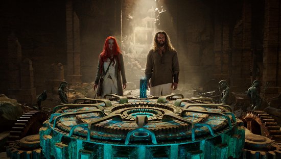 Man en vrouw met rode haren staan voor een groot, rond mechanisch object met blauwe lichten.