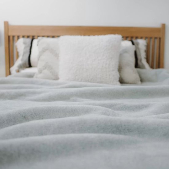 Lichtgrijze wollen deken over een bed met houten hoofdeinde en kussens.