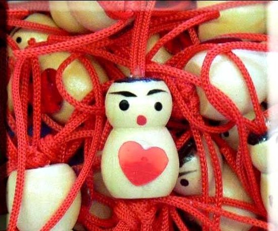 Een gelukspoppetje met een rood hartje en rode touwtjes.