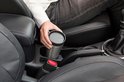 Vrouw plaatst een roestvrijstalen thermosbeker met grijs deksel in de bekerhouder van een auto.